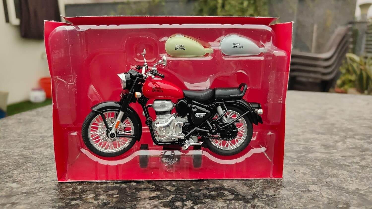 High-quality miniature replica of a Royal Enfield motorcycle in red, displayed with its retail box and two additional colored fuel tanks, offering pull-back action for interactive play from Usmile Toys www.usmile.toys